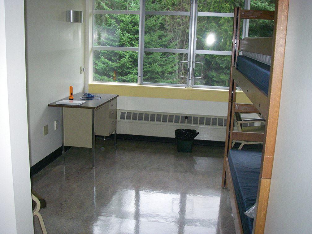 Dormitory room, including a bunk bed, desks and a large window overlooking trees.