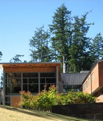 A glass and wood building sits on a grassy hill, with pine trees in the background.